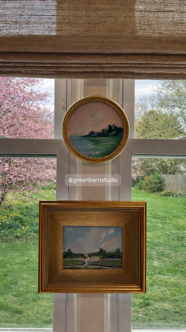Landscape paintings in gilt frames hung against a garden window