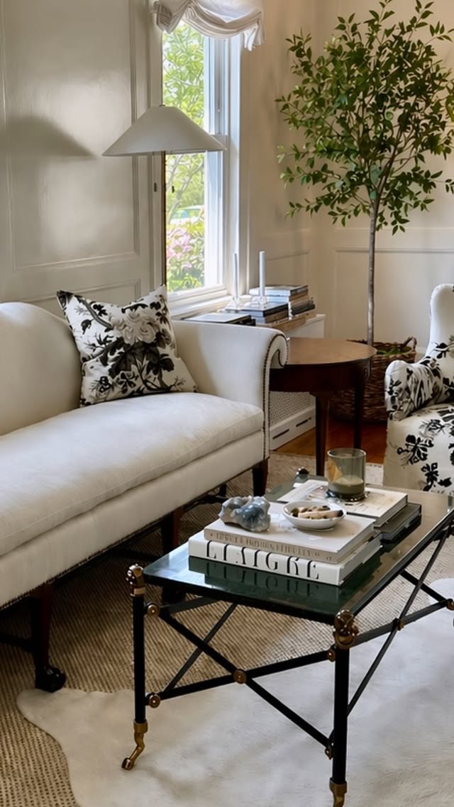 Cream camelback sofa with black floral pillows and a marble-top coffee table